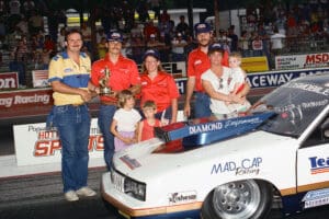Race car team celebrating with trophy and children.