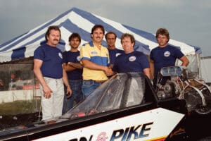 Race team posing with dragster car.