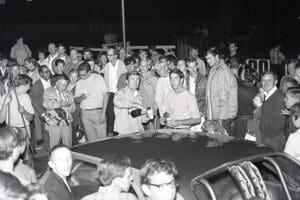 Crowd gathered around a car at night.