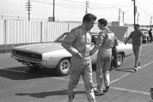 Men in racing suits beside classic car.