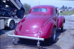 Red vintage car parked on gravel lot.