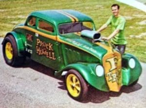 Man with vintage green race car outdoors.