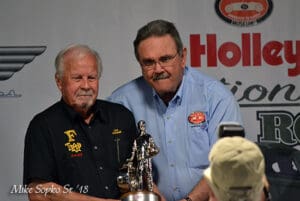 Two men holding a trophy together, smiling.