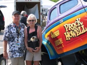 Couple with dog beside colorful vintage car.