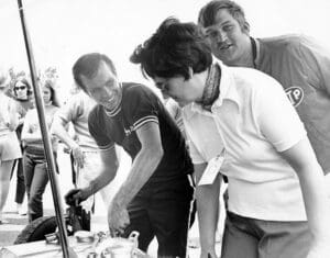 People gathered around a car engine, smiling.