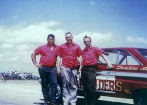 Three men in red shirts by car.