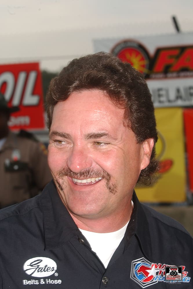 Man smiling at outdoor event with banners.