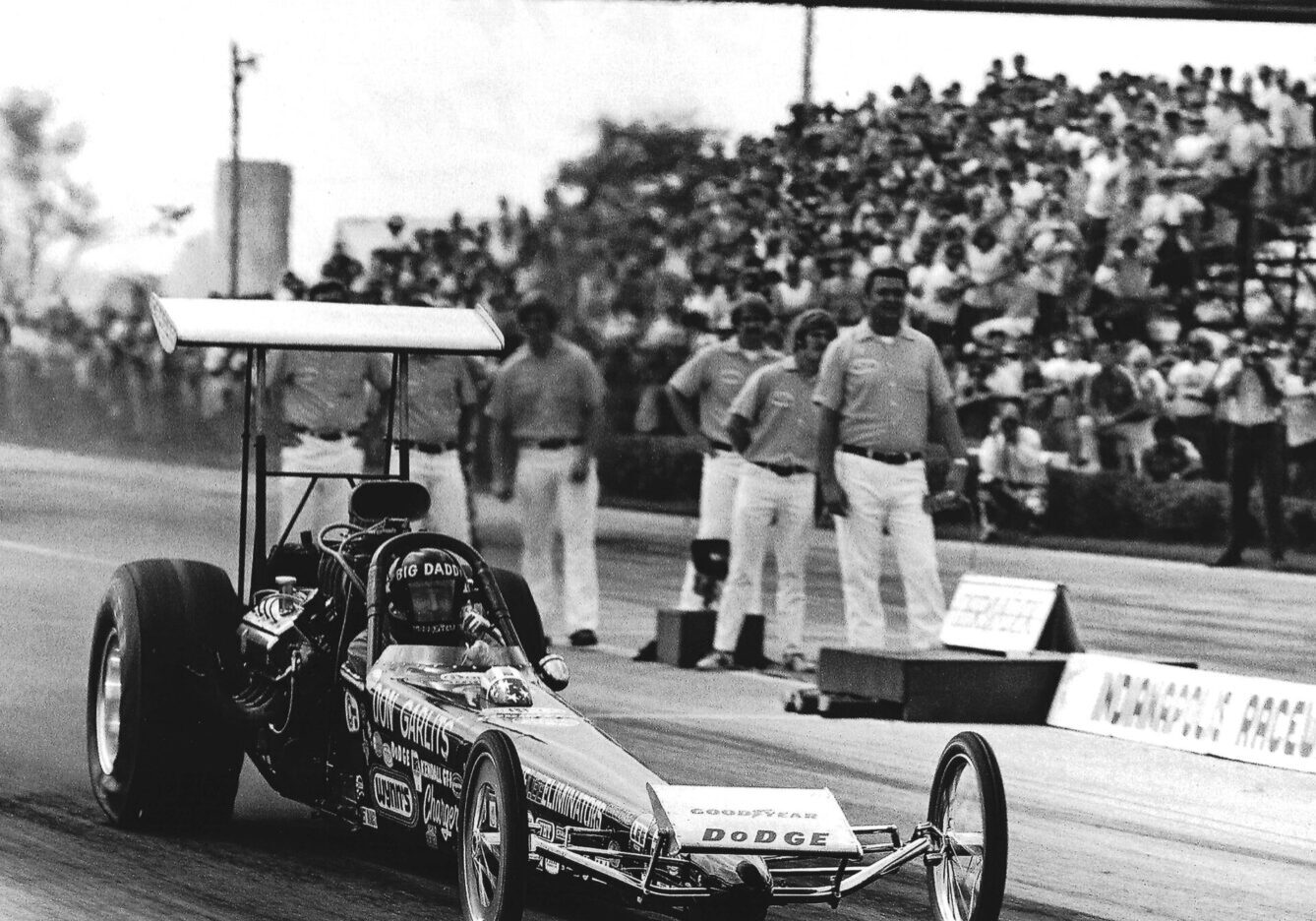 An old photo capturing the essence of drag racing as a man fearlessly drives his drag car.