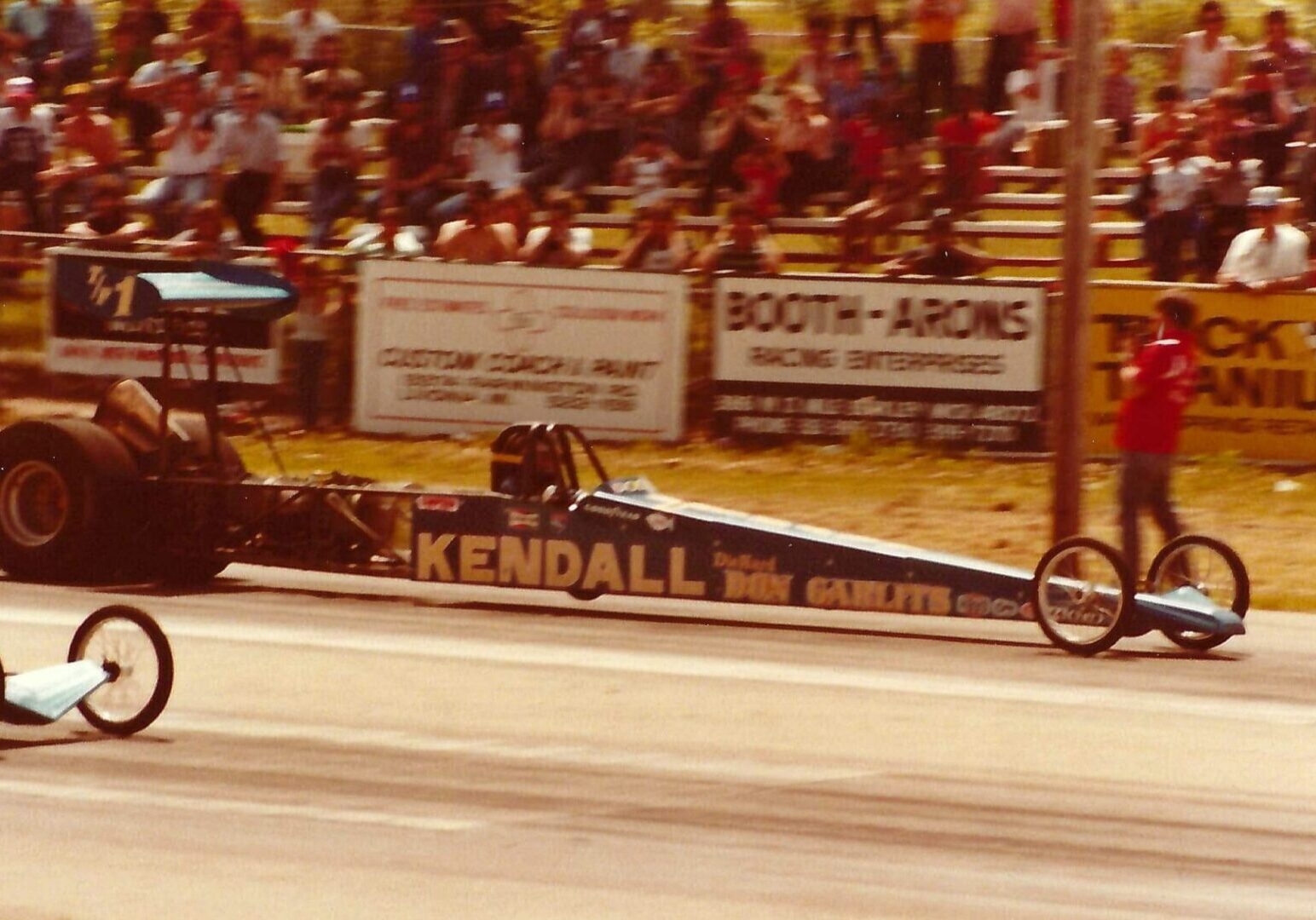 A drag car racing down a track with spectators in the stands.