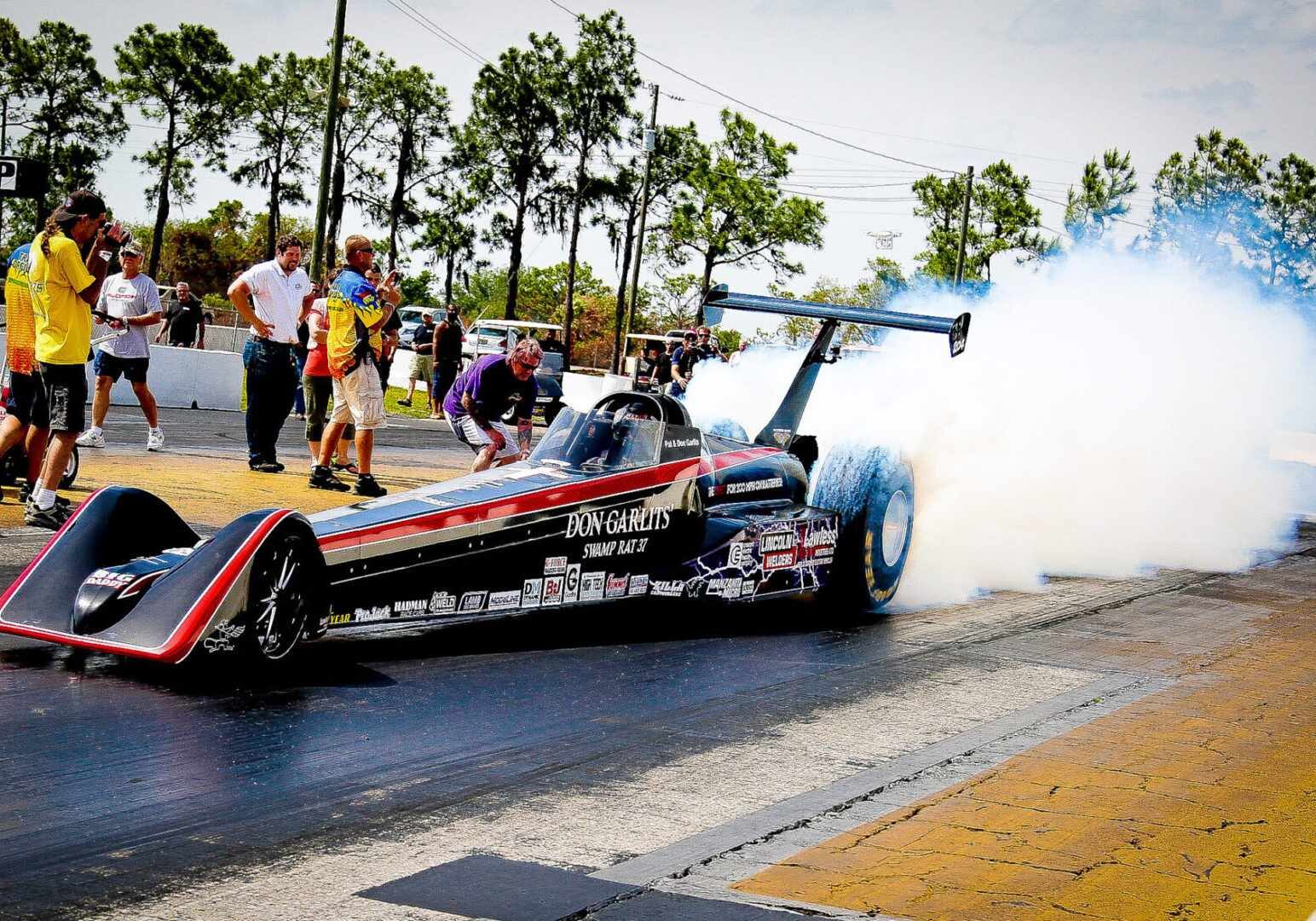 A high-performance drag racing car emitting billows of smoke as it accelerates down the track.