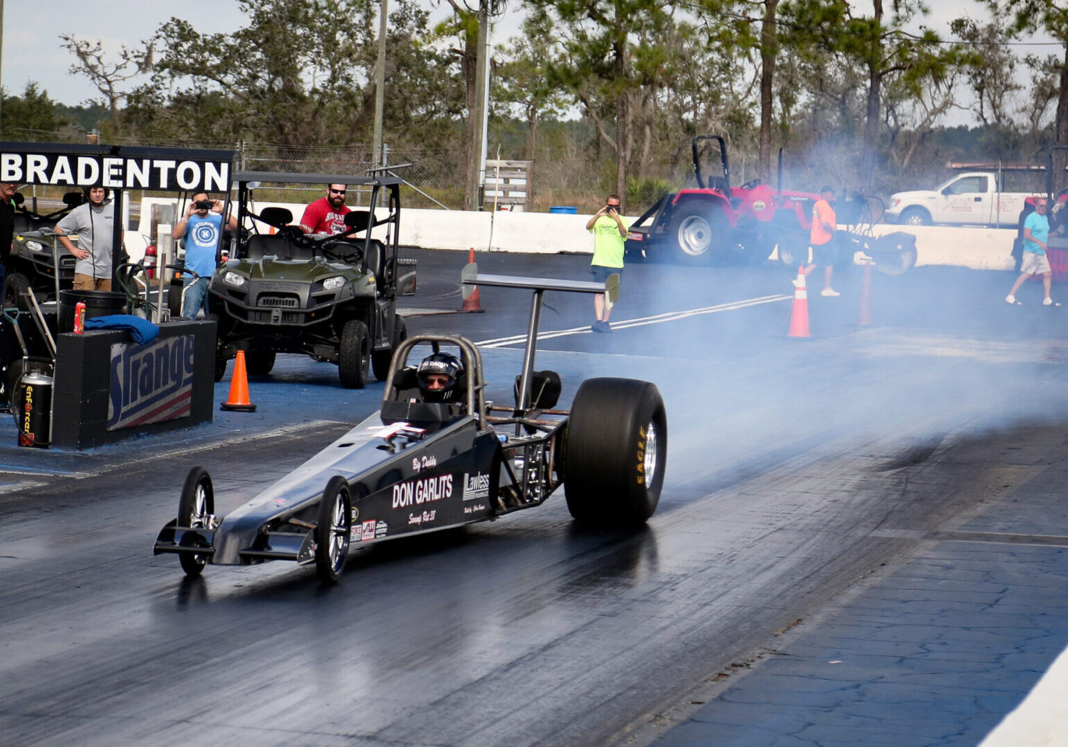 A man participating in drag racing, driving a drag car on a track.