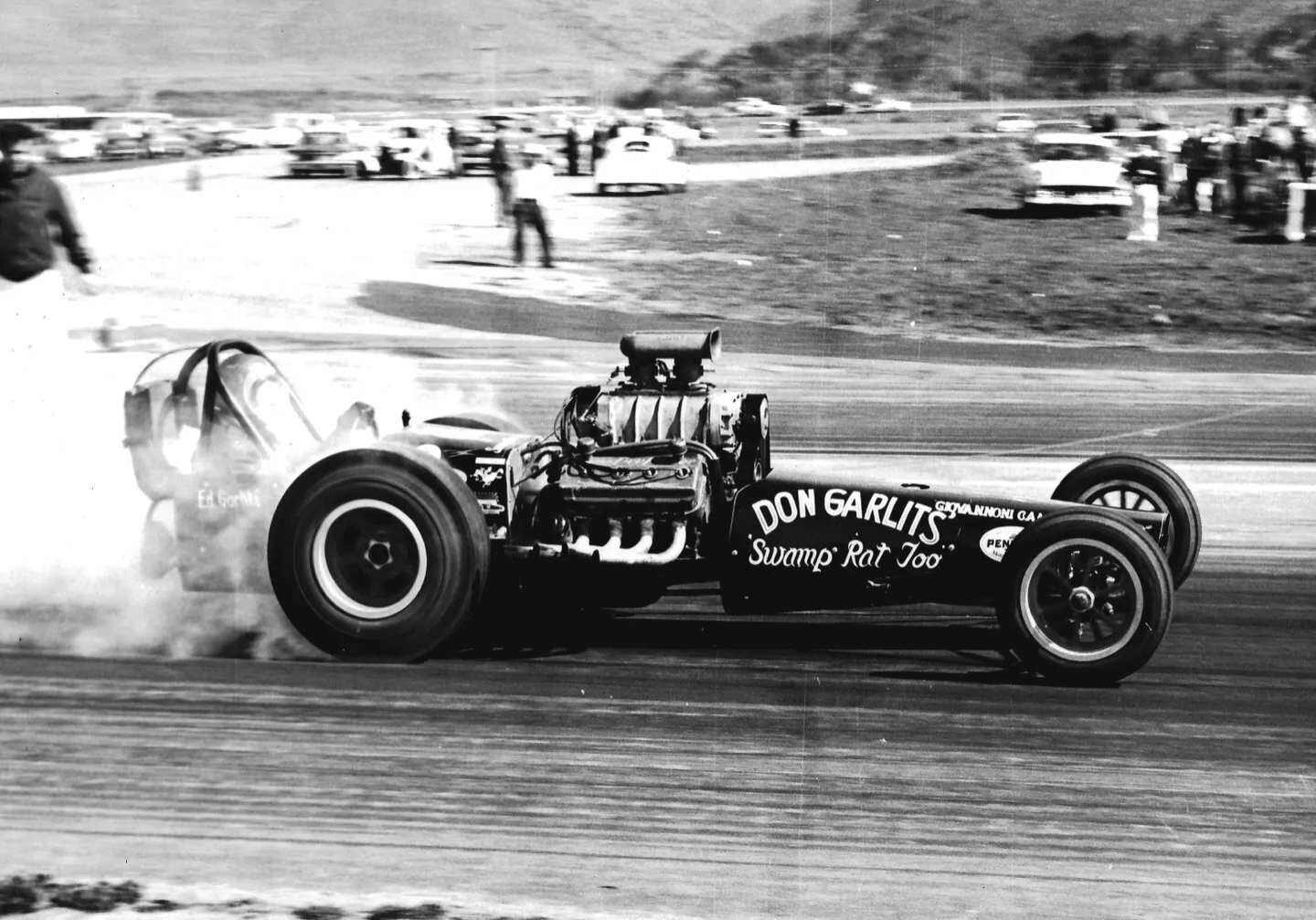 A black and white photo of a drag car with smoke billowing out of it during a thrilling drag race.